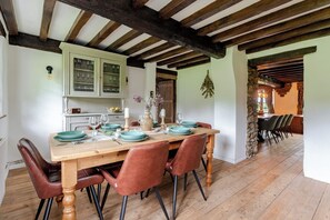 A dining area with a wooden table, chairs, and a stone wall. - 1641 Historic Farmhouse, Sleeps 16 · Bath/Bristol (Keynsham)