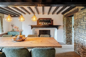 A rustic dining area with a wooden table, green upholstered chairs, and hanging pendant lights. - 1641 Historic Farmhouse, Sleeps 16 · Bath/Bristol (Keynsham)