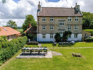 A stone building with a tiled roof, multiple windows, and a well-maintained lawn with outdoor seating. - 1641 Historic Farmhouse, Sleeps 16 · Bath/Bristol (Keynsham)