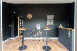 A bar area with two stools, a small round table, and a shelf with bottles. - 1641 Historic Farmhouse, Sleeps 16 · Bath/Bristol (Keynsham)
