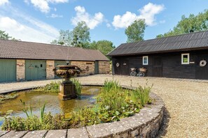 A courtyard with a fountain, stone walls, and a wooden building with a bicycle. - 1641 Historic Farmhouse, Sleeps 16 · Bath/Bristol (Keynsham)