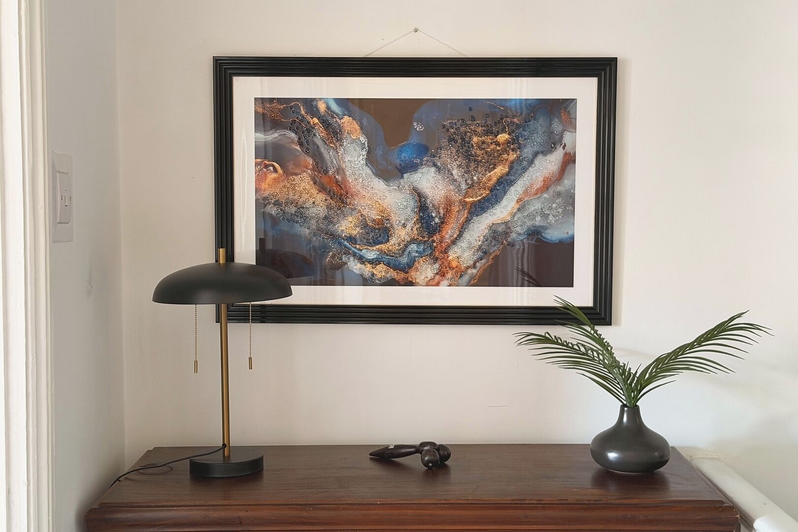 Ein gerahmtes abstraktes Gemälde an der Wand, eine Stehlampe, ein kleiner Tisch mit einer Pflanze und ein Headset auf dem Tisch.