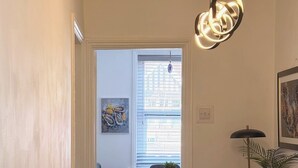 Ein Flur mit einer Treppe, die zu einem Zimmer mit Schreibtisch, Stuhl und einem Fenster mit Jalousien führt.