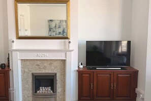 A fireplace with a stone surround, a mounted television on a wooden cabinet, and a framed artwork above the fireplace. - The M4 Escape | J26 | Free Parking | Newport (Newport)