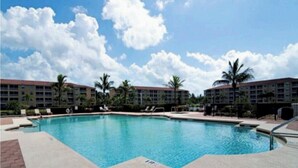 A swimming pool with lounge chairs and palm trees, surrounded by multi-story buildings. - Wake Up to Sunshine in This Beautiful 2bed/2Bath Southwest Florida Condo! (Fort Myers)
