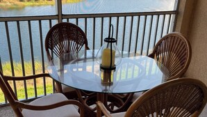 A glass-top table with wicker chairs, a candle, and a view of a lake and buildings. - Wake Up to Sunshine in This Beautiful 2bed/2Bath Southwest Florida Condo! (Fort Myers)