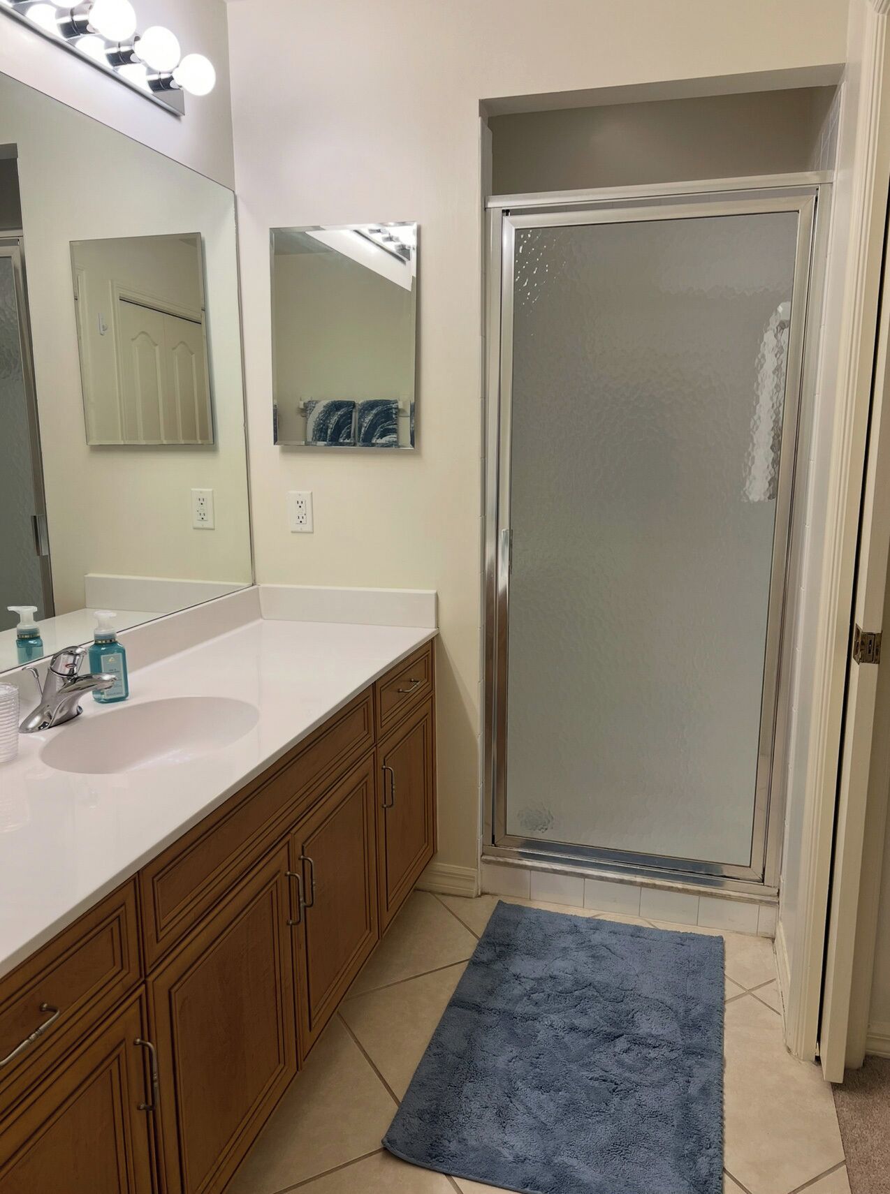A bathroom with a white sink, wooden cabinets, a blue rug, and a glass shower enclosure.