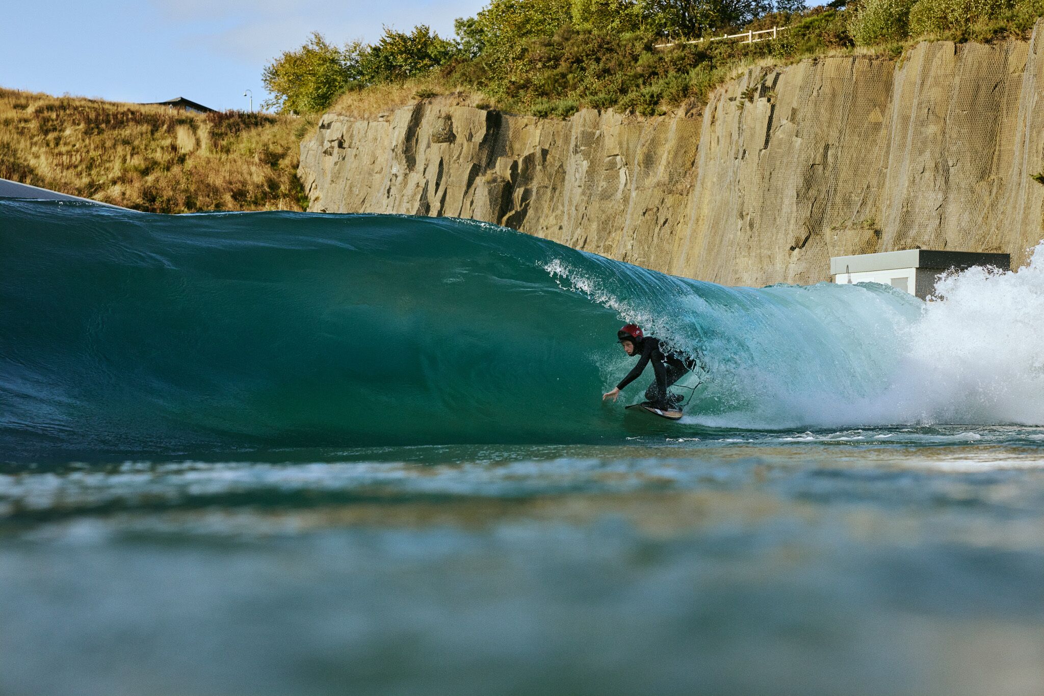 Ein Surfer reitet auf einer hohen Welle, im Hintergrund eine felsige Klippe.