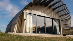 Un edificio moderno con tetto curvo, ampie finestre in vetro e rivestimento in legno.