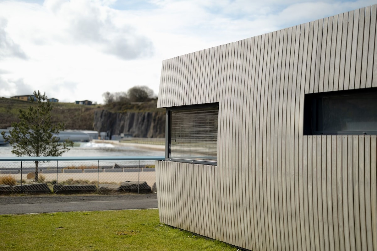A modern building with a ribbed exterior, a large window, and a view of a water body.