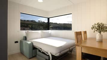A compact room with a bed, a dining table, and a window offering a view of a landscape.