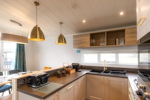 A modern kitchen with a built-in oven, a sink, and a dining area with a table and chairs. - Lost Shore Surf Resort (Newbridge)