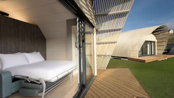 A modern bedroom with a bed, a seating area, and a view of a unique architectural structure.