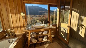 Un baño de cabaña de madera con una ventana grande, un lavamanos, un espejo y una ducha.