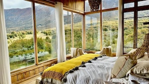Un dormitorio con una cama grande, vistas a un paisaje montañoso y techo de madera.