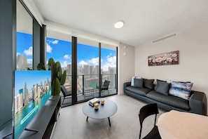 A modern living room with a large window, a sofa, a coffee table, and a flat-screen TV. - Luxury 2BR | Downtown Miami Condo | Rooftop Pool (Miami)