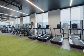 Ein Fitnessraum mit Laufbändern, Ergometer und einem Teppichbereich in Grün.