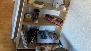 En hylla i trä med köksredskap, en tekanna, en vattenkokare, en kaffebryggare och några böcker.