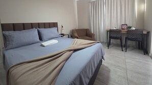 Habitación de hotel con cama, escritorio, silla, mesita de noche y ventilador de techo.