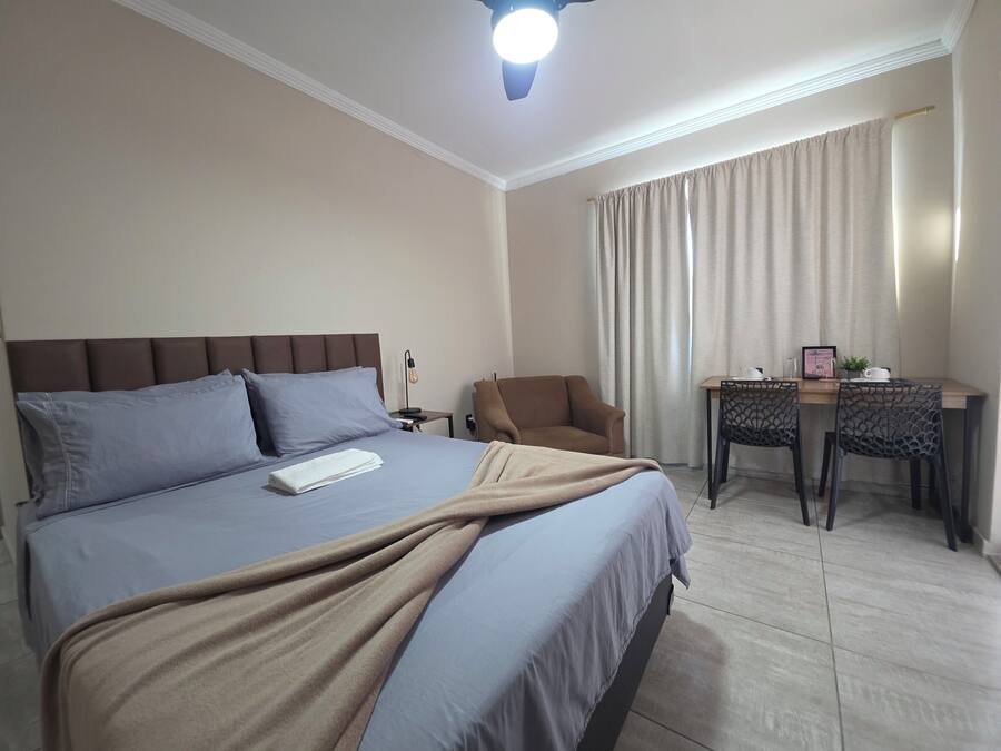 A hotel room with a bed, a desk, a chair, a nightstand, and a ceiling fan.