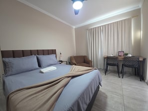 A hotel room with a bed, a desk, a chair, a nightstand, and a ceiling fan.