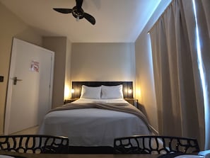 A hotel room with a bed, bedside tables, a ceiling fan, and a door with a sign.