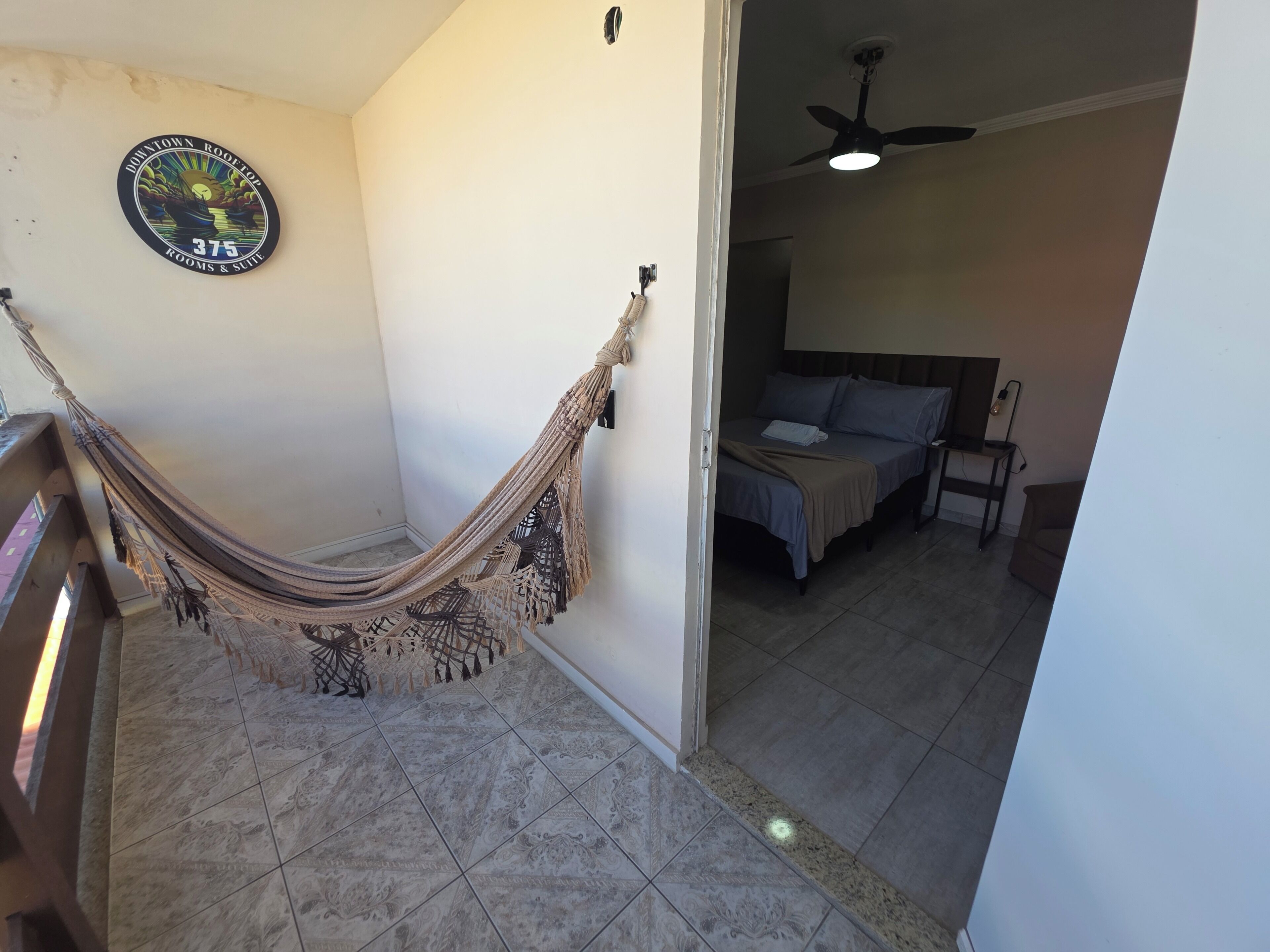 A room with a hammock, a bed with pillows, a ceiling fan, and a wall with a logo.