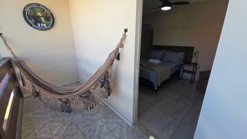 A room with a hammock, a bed with pillows, a ceiling fan, and a wall with a logo.