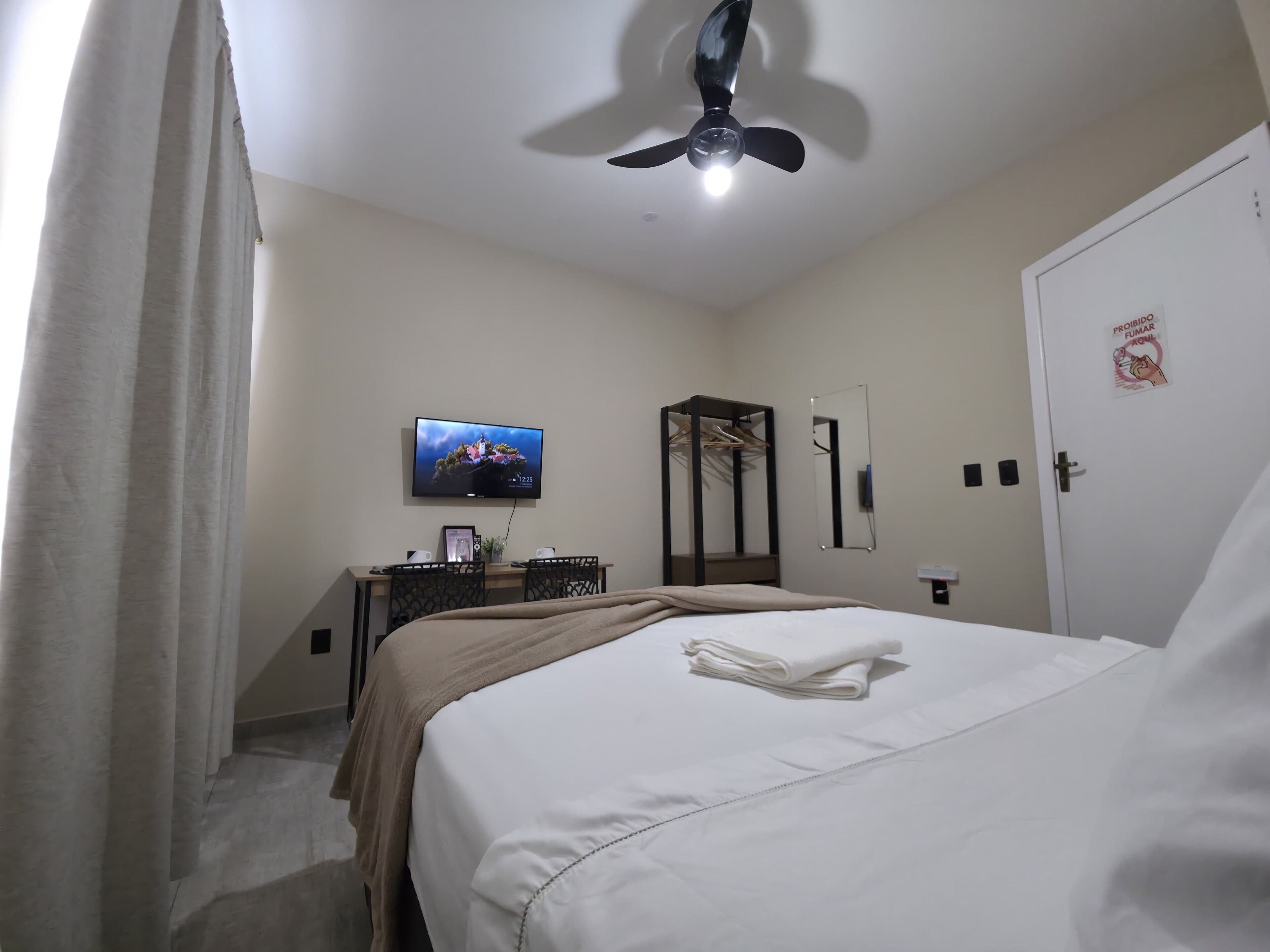 A hotel room with a bed, a desk, a television, a mirror, and a door.