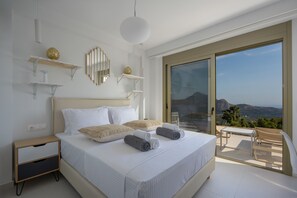 Une chambre avec un grand lit, des tables de chevet, une vue sur l’extérieur grâce à une porte-fenêtre coulissante, et un balcon avec une table et une chaise.