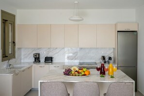 Eine moderne Küche mit Marmorarbeitsplatten, einer zentralen Kochinsel mit Obst und Getränken sowie einem Edelstahl-Kühlschrank.