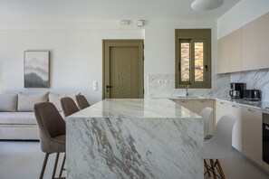 A modern kitchen with a marble island, a dining area with chairs, a sofa, and a painting on the wall. - Aurea Kalithea Sunset  Sunrise  Sea (Asomatos)