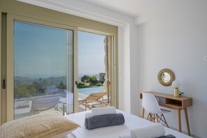 Habitación de hotel con cama, escritorio, silla y un amplio ventanal corredero que da a un balcón con piscina y vistas al paisaje.