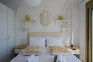 A neatly arranged hotel room with a bed, bedside tables, and wall-mounted shelves with decorative items. - Aurea Kalithea Sunset  Sunrise  Sea (Asomatos)