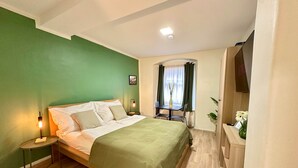 A bedroom with a bed, bedside tables, a window with curtains, a small table with chairs, and a mirror. - Compact Apartment on Lendplatz | Self-Check-In (Graz)