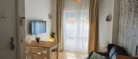 Una sala de estar con sofá, televisor, mesa de comedor con sillas y una puerta corrediza de vidrio.