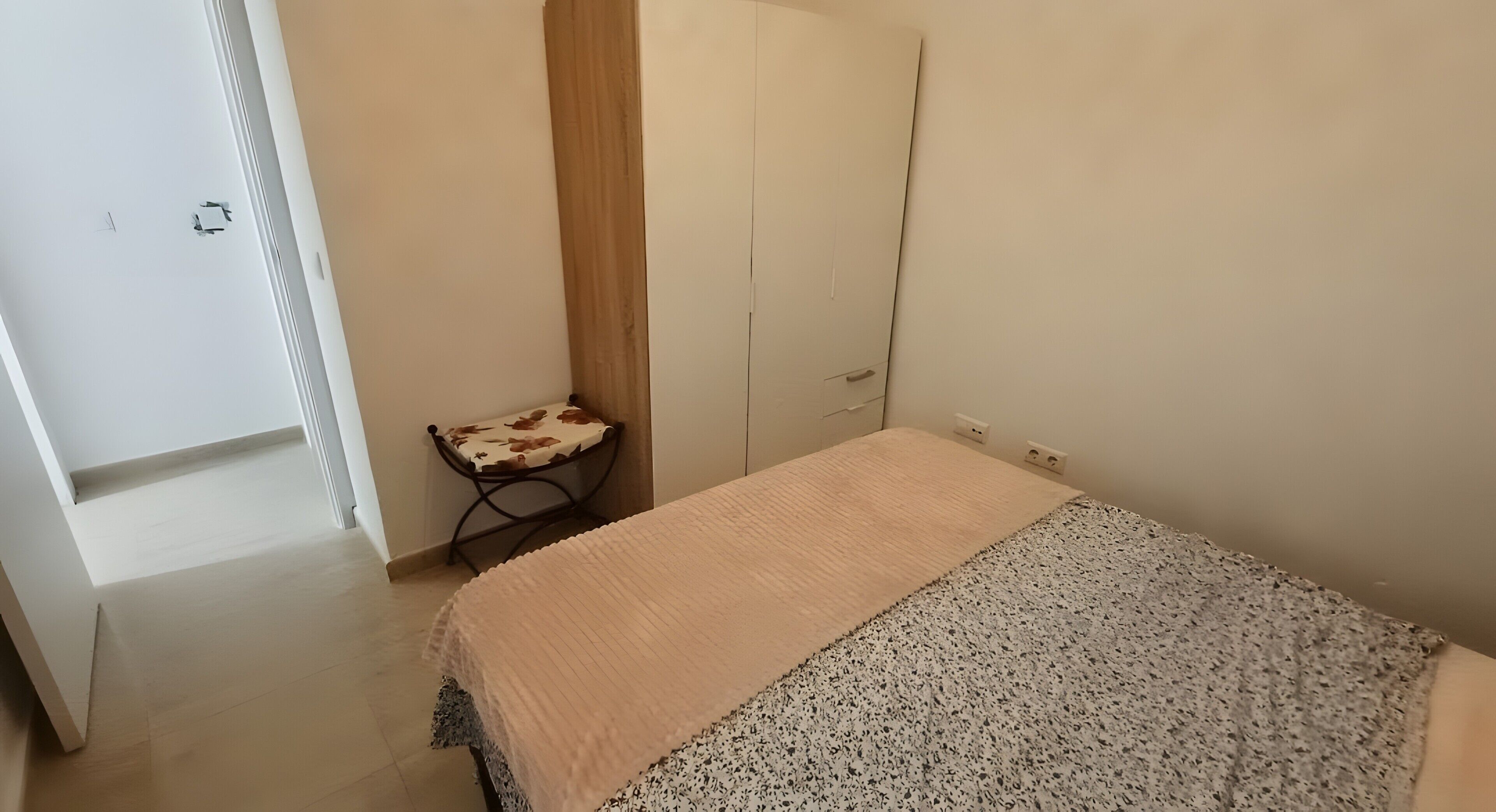 Un dormitorio con cama, armario, una mesita con silla y una puerta.