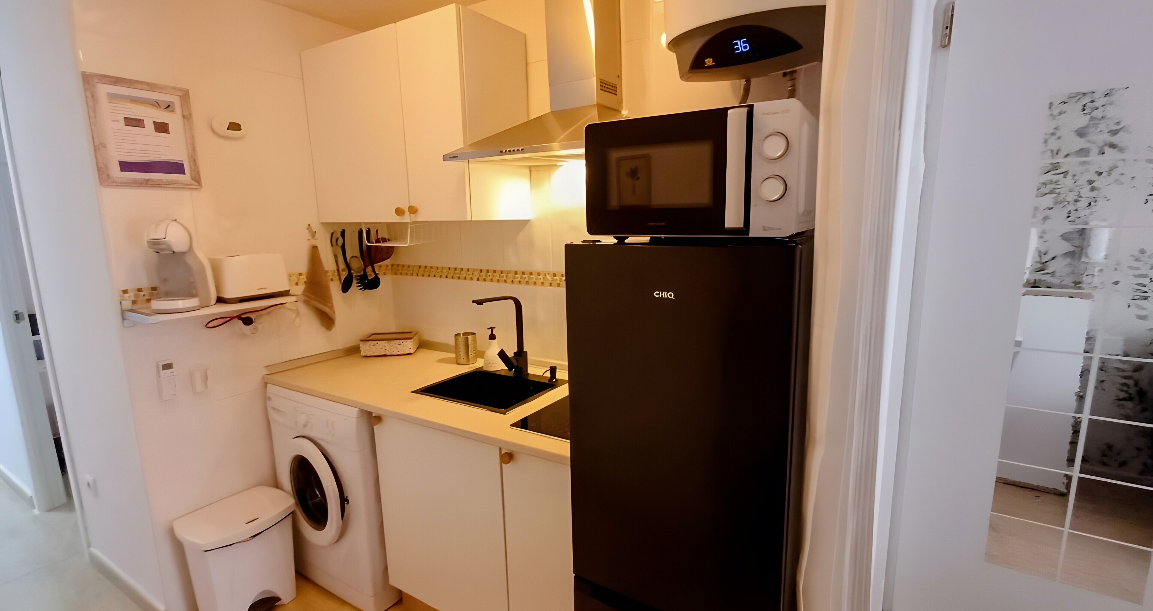 A compact kitchen with a washing machine, a microwave, and a refrigerator.