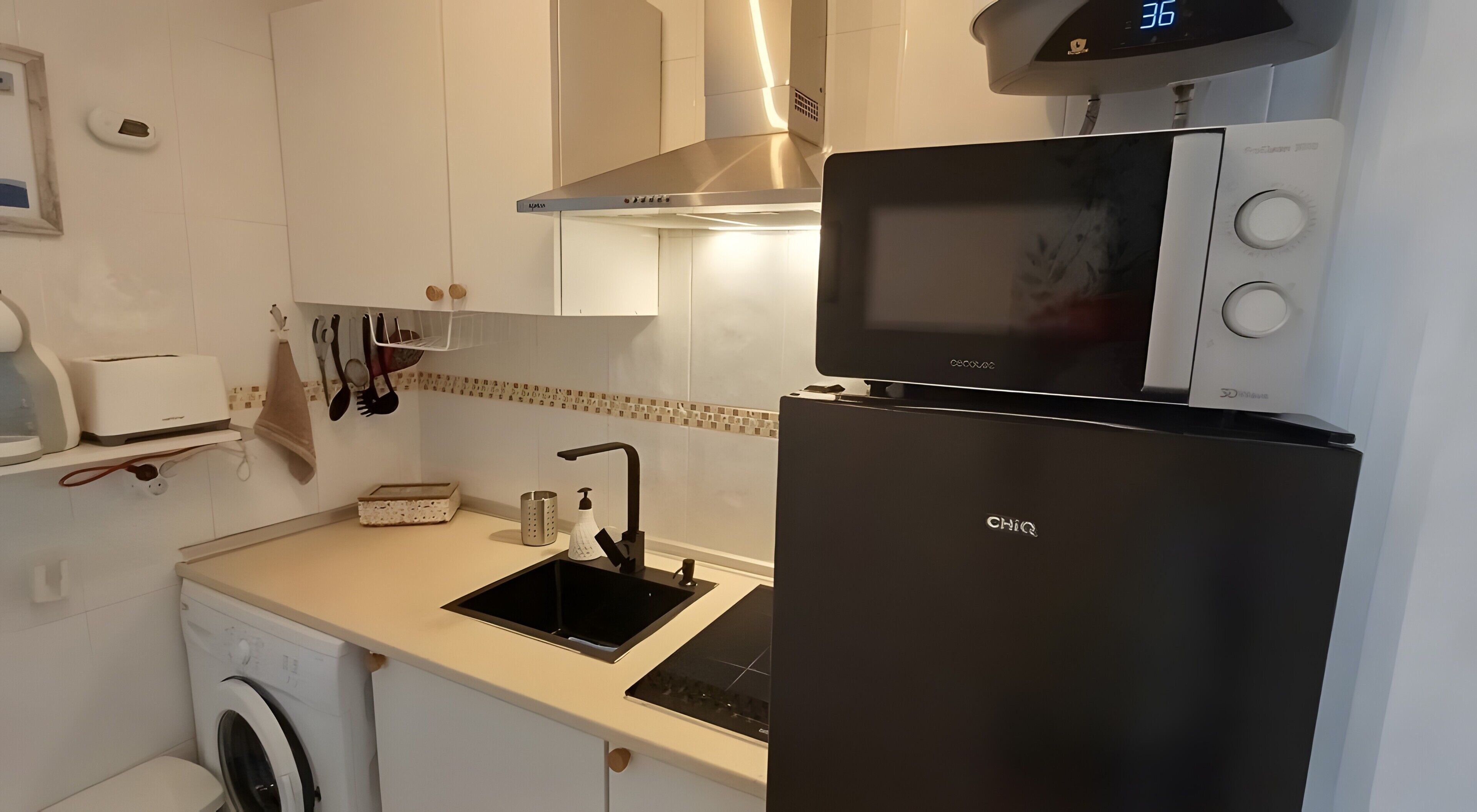 Eine kleine Küche mit Waschmaschine, Mikrowelle und Kühlschrank.