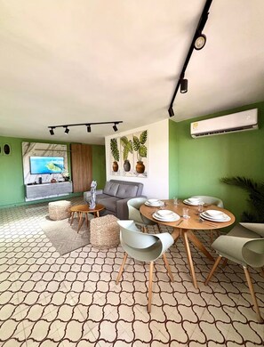 A modern living room with a sofa, a dining table set for four, and a television.