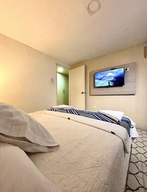 A hotel room with a bed, a television mounted on the wall, and a door leading to another room.