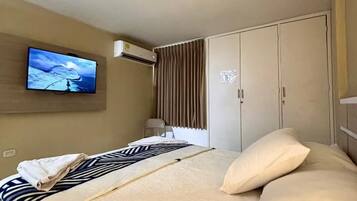 Habitación de hotel con cama, televisor montado en la pared, armario y aire acondicionado.