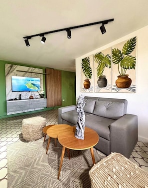 A living room with a grey sofa, a wooden coffee table, and a TV mounted on a green wall.