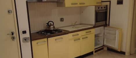 A compact kitchen with a gas stove, a kettle, a sink, and a built-in oven.