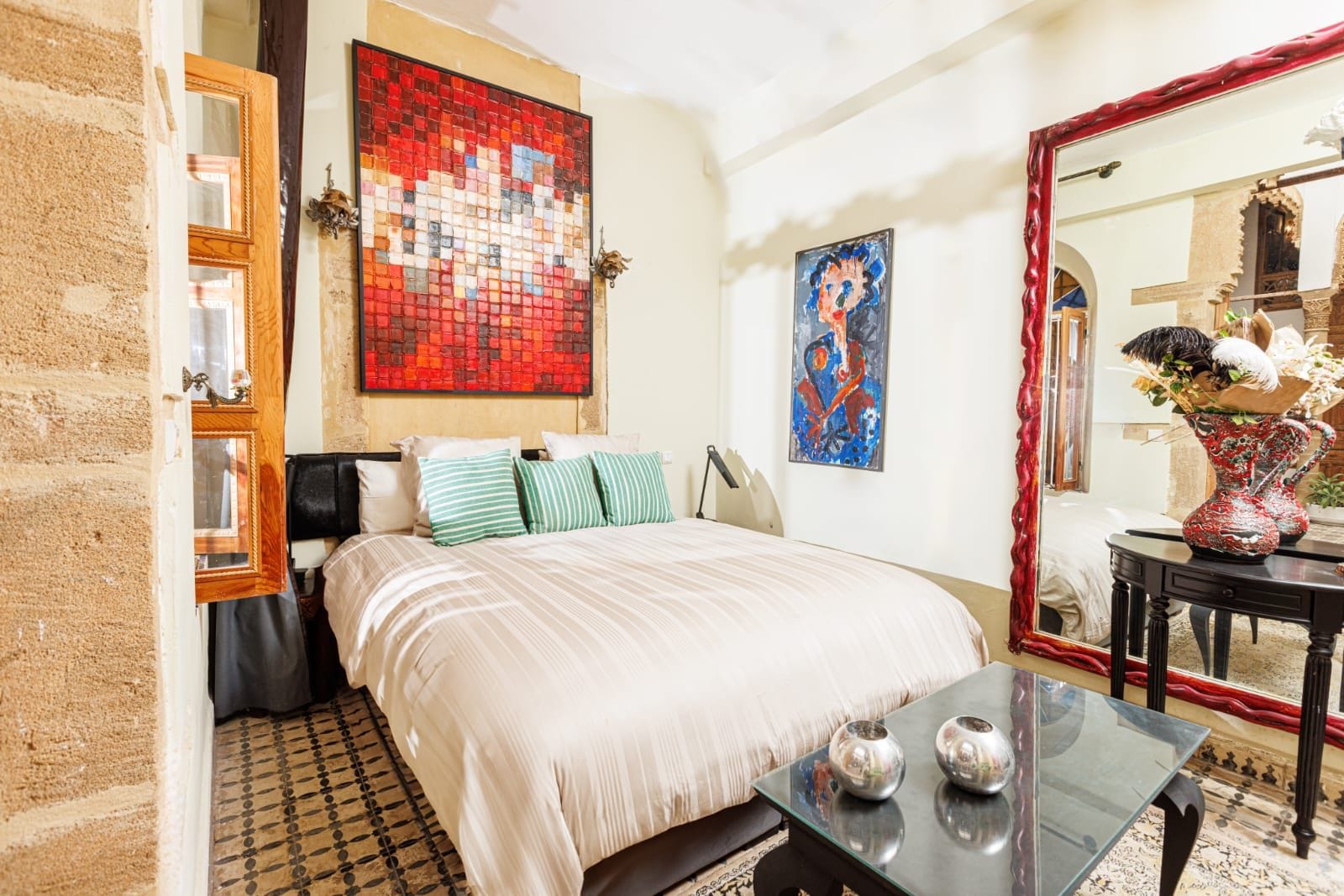 A hotel room with a large bed, a mirror, and two paintings on the wall.