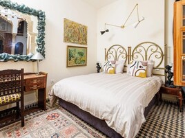 Un dormitorio con cama, mesita de noche, lámpara, espejo y alfombra estampada.