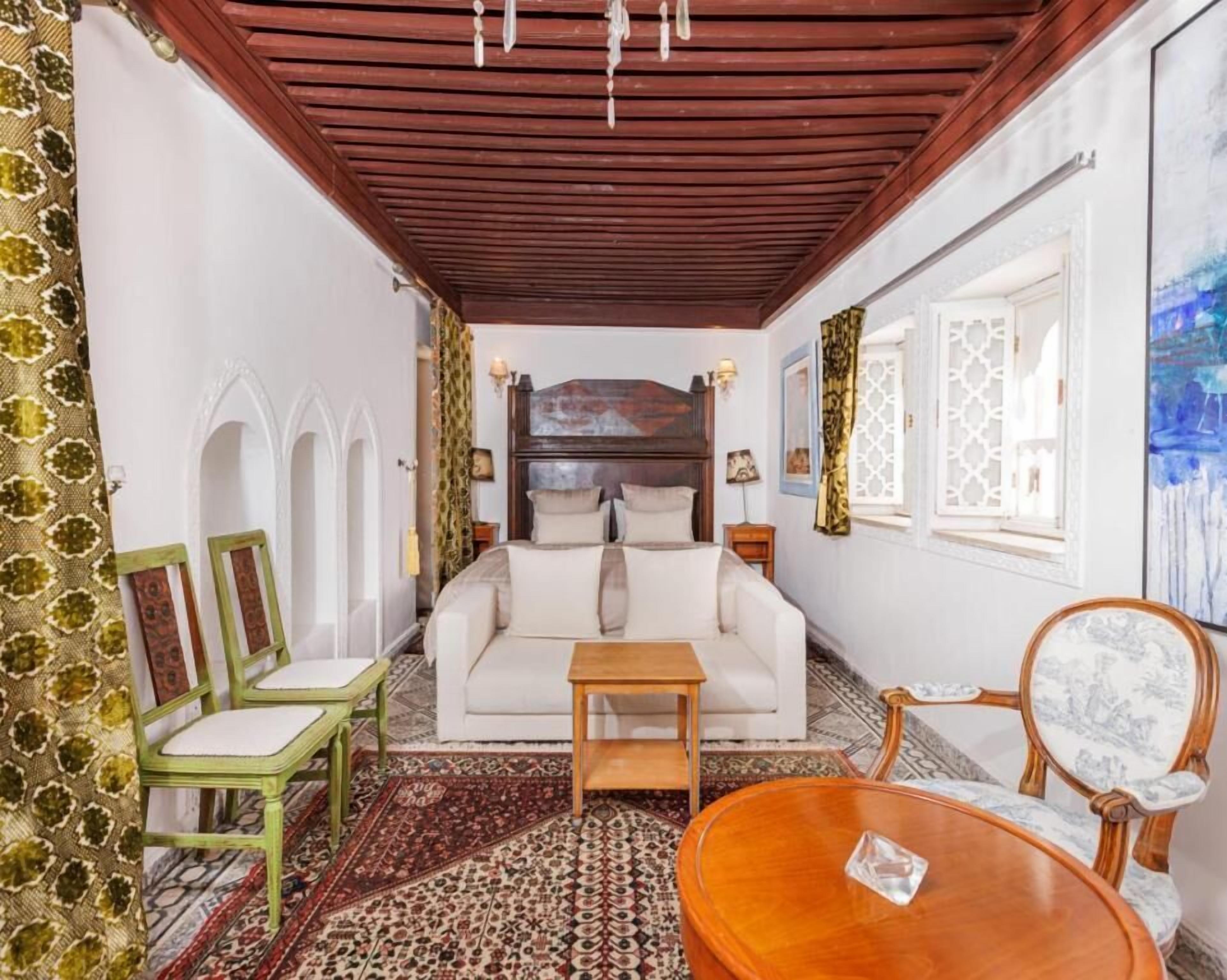 Een kamer met een houten plafond, een witte bank, een houten salontafel en gordijnen met een patroon.
