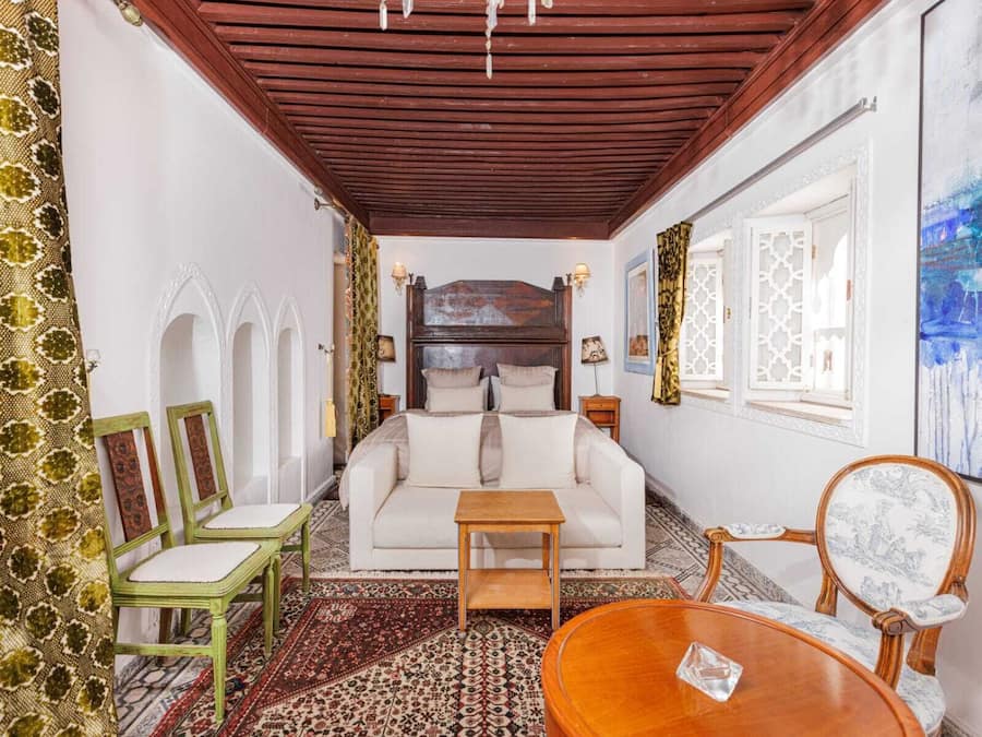 Quarto com teto de madeira, sofá branco, mesa de centro de madeira e tapetes estampados.