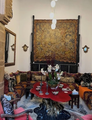 A traditional living room with a large tapestry, ornate sofas, a red round table, and a decorative mirror. - Dar Tya  (Salé)