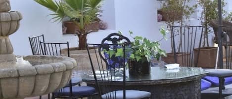 A poolside area with a stone fountain, a table with chairs, and potted plants.